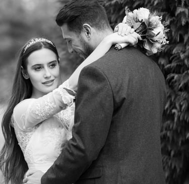 black and white photo of bride and groom, bride looking into distance, groom looking at bride and smiling, blurry background