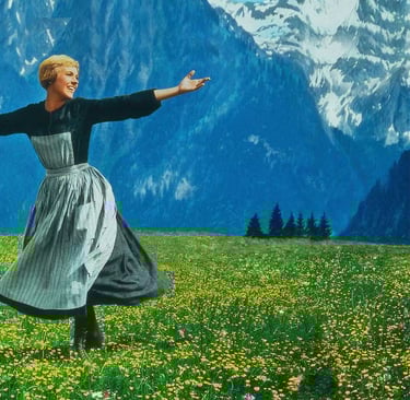 Julie Andrews as Maria stands arms wide on a mountain in The Sound of Music