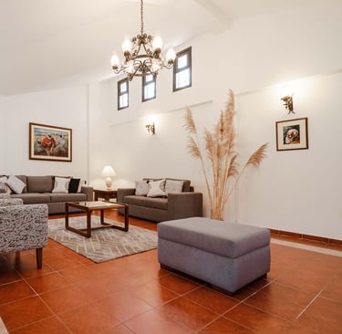 Habitación interior amoblada y decorada con pinturas, candelabro plantas con sillones cafés AirBnB en Quito, Ecuador