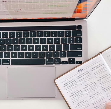 An open calendar planner, slightly laid over the keyboard of an open laptop.