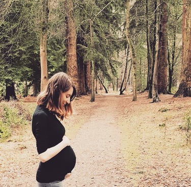 pregnant woman standing in a forest holding her bump