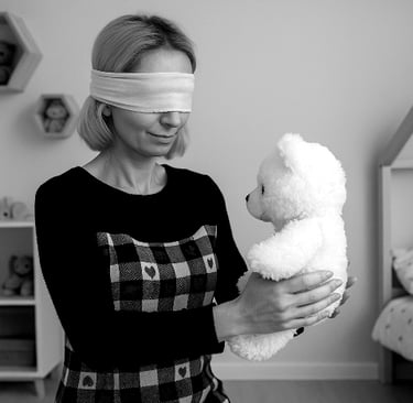 Kobieta z opaską na oczach stoi w jasnym, skromnym pokoju dziecięcym i delikatnie trzyma w dłoniach