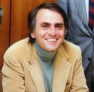 Carl Sagan in a suit and tie smiling at the camera