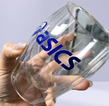 Hand holding a clear glass mug with a UV DTF printed 'Basics' sticker.
