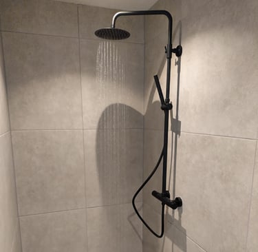 Zwarte douche in sobere badkamer met grote tegels.