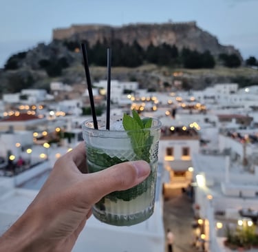 A refreshing mint mojito cocktail at a Lindos rooftop bar with the Acropolis of Rhodes in the background.