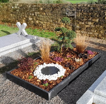 Sépulture moderne avec cadre en schiste, cercle de pierres blanches et paillis naturel.