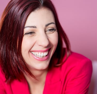 Portrait d’une comédienne qui rit, en veste rose sur fond rose, sourire naturel et expressif.