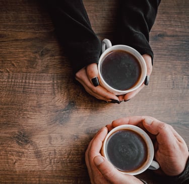 Two people holding cups of coffee meet to talk