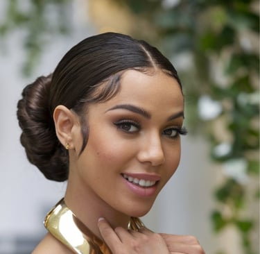 A woman wearing a sleek flat twist updo, accessorized with gold cuffs, smiling confidently at the camera.