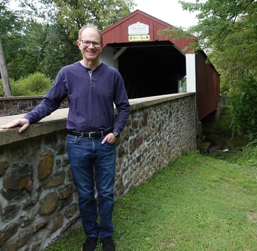 Picture of Michael leaning on a stone wall of a covered bridge in Pennsylvania