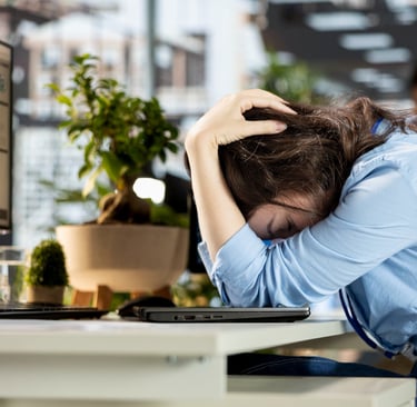 Stressed office worker resting head on desk, illustrating workplace burnout and mental health struggles.