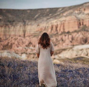 Woman in a beige dress standing in a lavender field with Cappadocia’s rock formations in the background