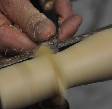 A close-up of a hand holding a chisel, turning wood spinning on a lathe
