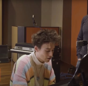 Jacob Collier sitting at the piano while Simon Sinek looks on in amazement.