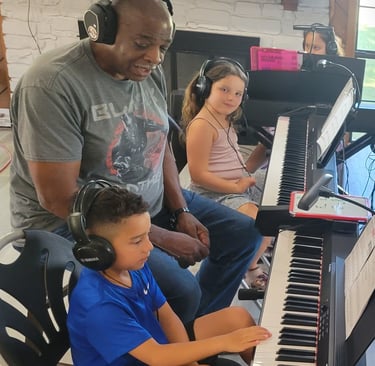 a group of kids sitting at pianos with a teacher