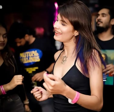 Smiling woman with purple hair highlights and a chest tattoo dancing at a crowded night club party.