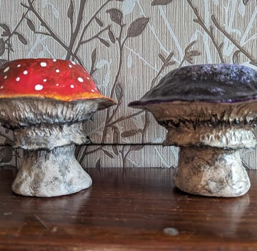 Hand-painted red amanita and purple clay mushroom figurines on a wooden shelf.