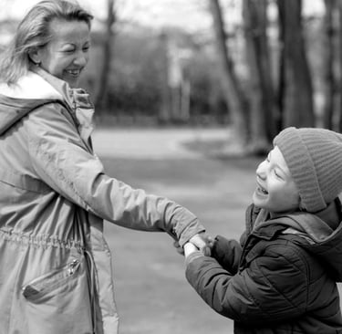 Usmiechnięty chłopiec z wadą wzroku wraz z mamą na ścieżce wśród drzew.