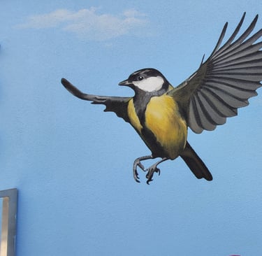 Fresque peinte sur une façade. Une mésange et une plume colorée s'envolent sur un ciel bleu.