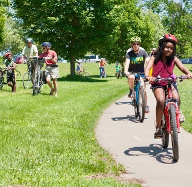 Two people riding bikes on a paved path through a green space