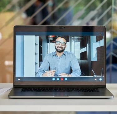 A laptop screen showing a video call with a man in a business shirt holding a pen