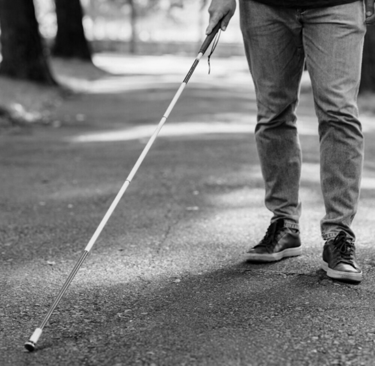Niewidomy mężczyzna porusza się za pomocą białej laski w ścieżce.