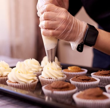 Photo of person piping icing onto a tray of cupcakes