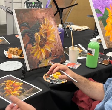 a man is painting a picture of a sunflower at an art-ish event