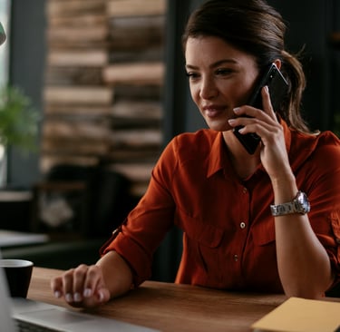 A woman in a red blouse, sitting at her desk talking on the phone.