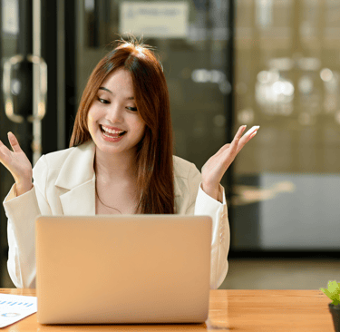 an ecstatic woman celebrating sitting at a table with a laptop and a plant