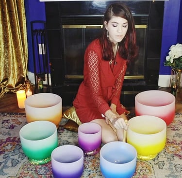 a woman sitting on a rug with crystal singing bowls and candles