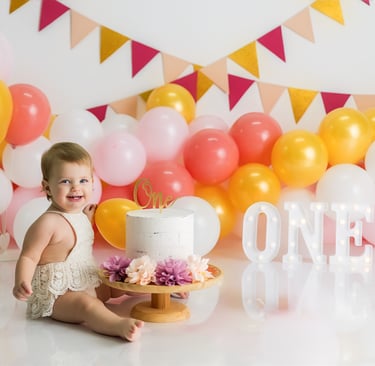 bebé sentada junto a tarta delante de globos en la sesión de smash cake