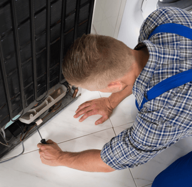 a man in a blue shirt is fixing a dishwasher