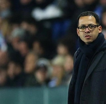 a man in a black coat and glasses on a soccer field
