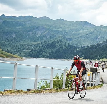 Un cycliste habillé en rouge trverse un barrage dans les Alpes, entouré de montagne