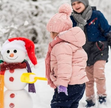a young child standing in the snow with a snowman