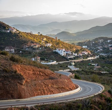 Winding road leading towards a Spanish mountain village and fading mountains in the background