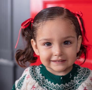 una niña pequeña con un suéter navideño sonriendo a la cámara 