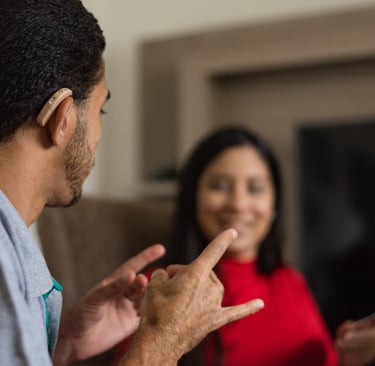 a deaf interpreter with a hearing aid in signing to someone on the couch