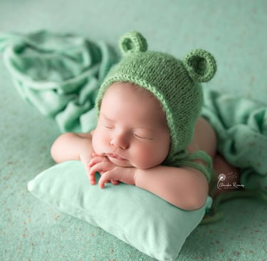 recién nacido con gorrito de orejitas sobre almohada verde