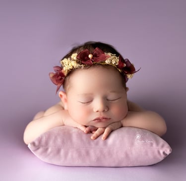 recién nacida con tocado dormida sobre almohada violeta