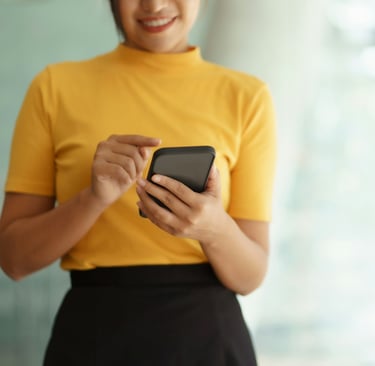 Woman in a gold top and dark brown skirt scrolling on a smart phone