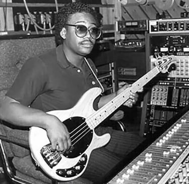 Black and white photo of Bernard Edwards holding a Music Man bass. He's sitting at a mixing console.