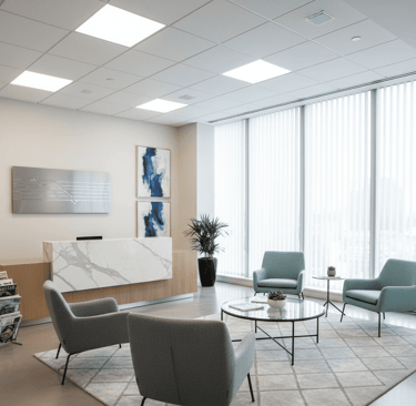 Recepção de consultório ou escritório moderna com balcão de mármore, área de espera com poltronas e grandes janelas.