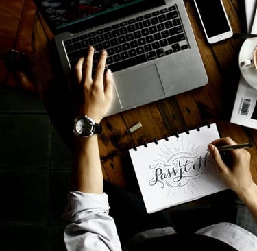 a person sitting at a table with a laptop, a notebook and coffee