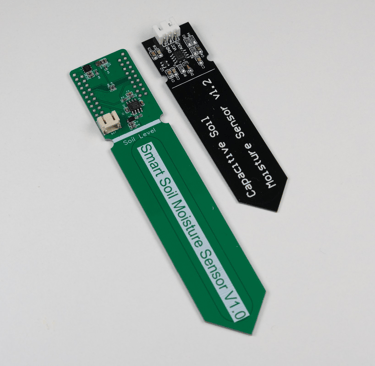 Our green PCB for complete plant monitoring next to a basic capacitive soil moisture sensor