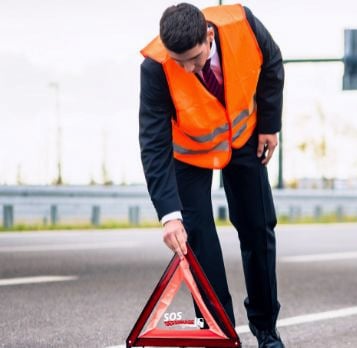 Un homme en gilet de sécurité se tient à côté d'une voiture en panne.