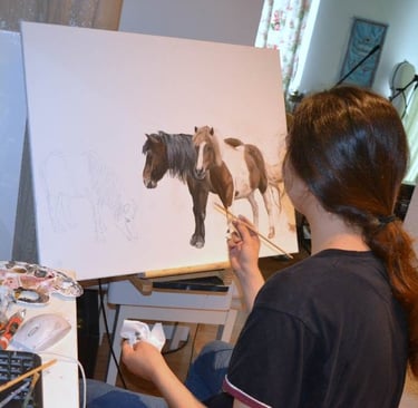 a woman is painting two ponies on a easel