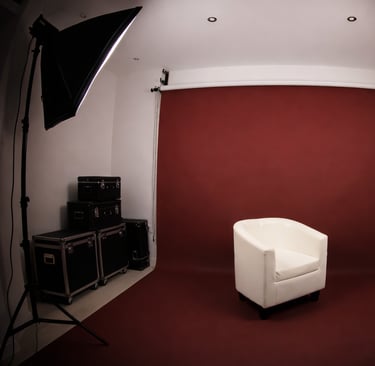 Studio photo avec fond couleu bordeaux fauteuil blanc au centre et deux softbox d’éclairage